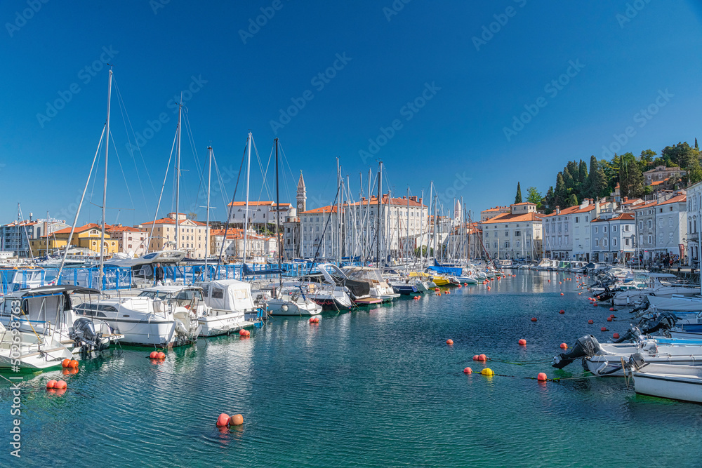 Mediterranean sunny port in slovenia, harbour view city of piran, old mediterranean houses and ships in the bay. Skyline with clocktower in back