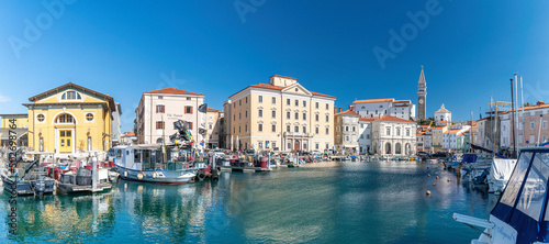 Mediterranean sunny port in slovenia, harbour view city of piran, old mediterranean houses and ships in the bay. Skyline with clocktower in back