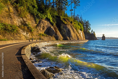 Siwash Rock, and the Seawall Bike Path, curved trail lines around Stanley Park with pine forested slopes of the Seawall on the Pacific coast. Pedestrians and cyclists on the trail