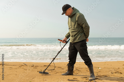 A man with a metal detector and a shovel on the seashore. A treasure hunter with a metal detector. A man is looking for a treasure. photo
