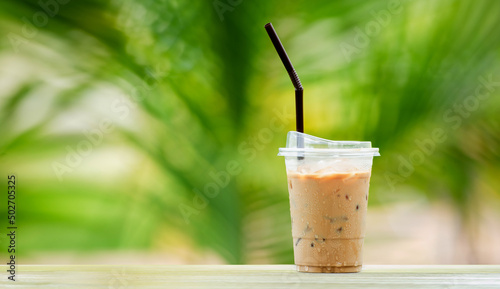 Iced coffee in tall glass, ice cubes. Cool summer drink with straws on warm natural green blur background. copy space