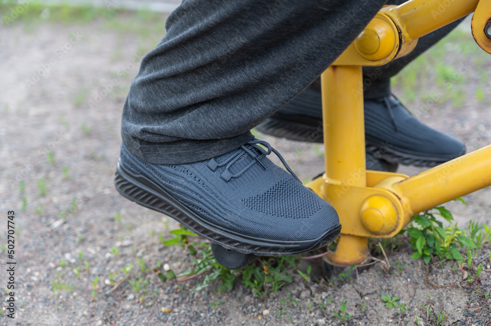 Close-up of a man's legs working out on the playground. Mature man in gray sweatpants and sneakers. Yellow sports equipment on the playground in the open air. Close-up of a man's legs working out on the playground. Mature man in gray sweatpants and sneakers. Yellow sports equipment on the playground in the open air.