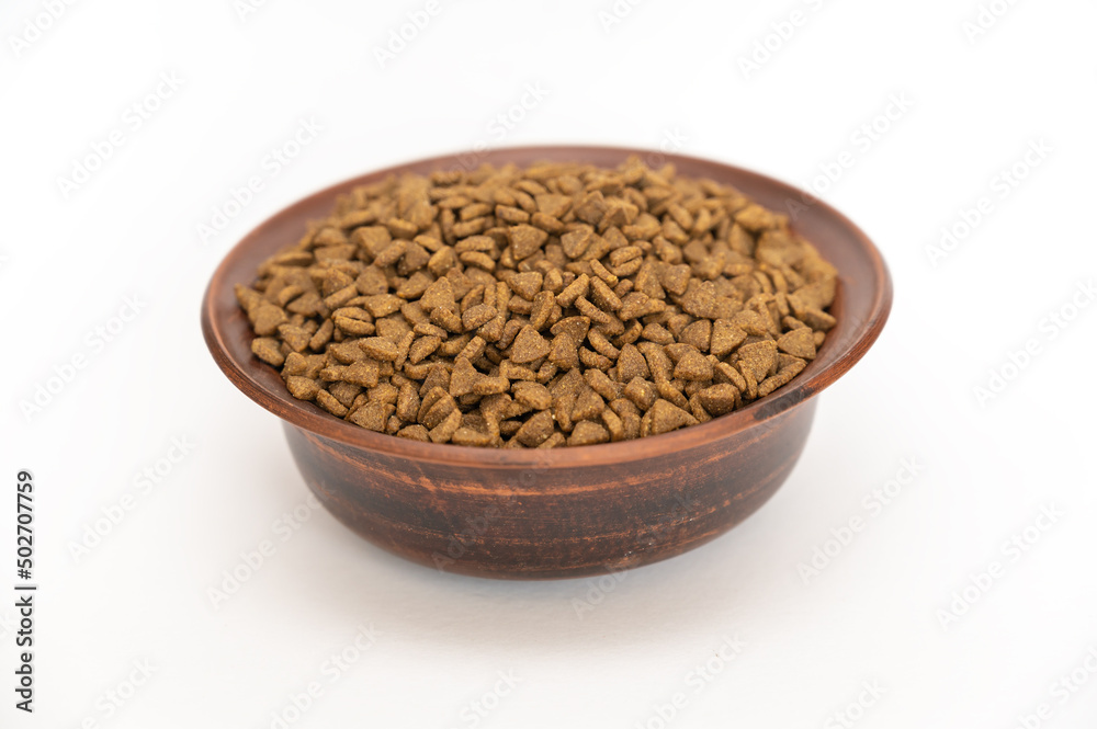 Pet food. Dry pelleted food in a brown clay bowl against a white background. The pellets are triangular. Pet food. Dry pelleted food in a brown clay bowl against a white background. The pellets are triangular.