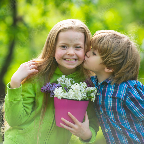 Two little children hug and kiss each other in summer garden. Kids couple in love. Friendship and childhood. Little girl kissing little boy outdoors in park.