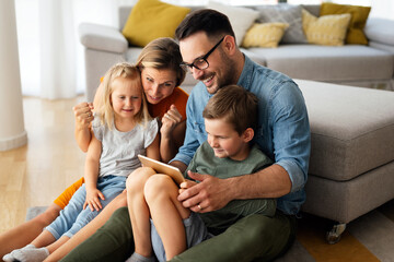 Happy young family having fun time at home. Parents with children using digital device.