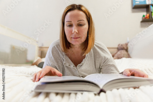 Smiling woman lies on the bed and reads a book. Recreation and education. © Анна Демидова