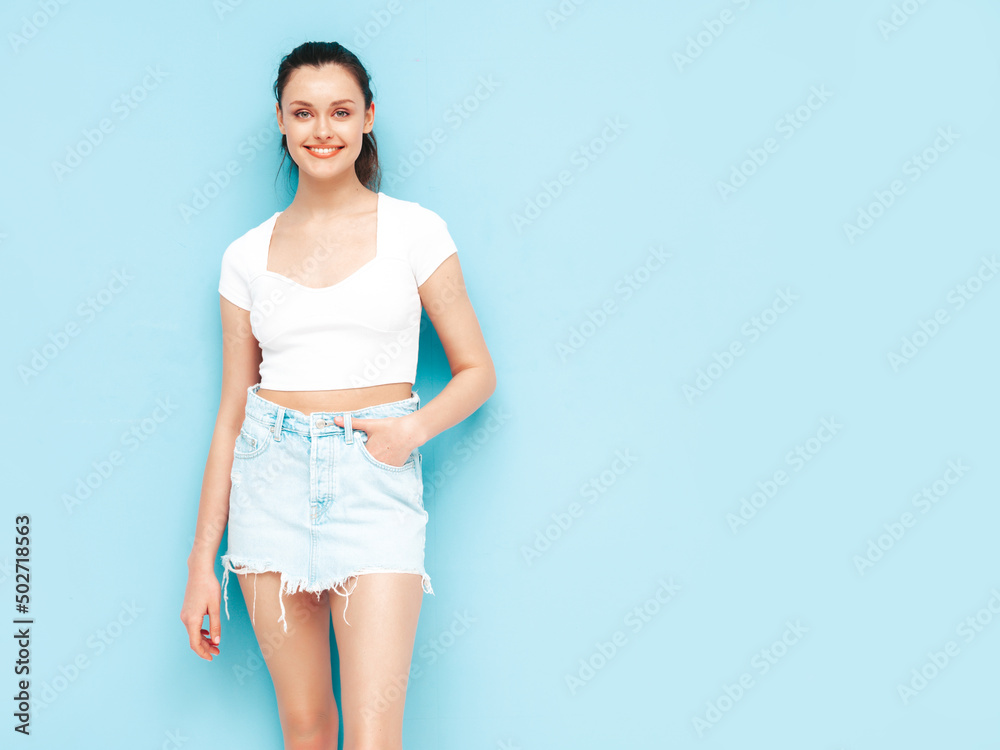 Young beautiful smiling female in trendy summer jeans skirt and top clothes. Sexy carefree woman posing near blue wall in studio. Positive brunette model having fun.Cheerful and happy Young beautiful smiling female in trendy summer jeans skirt and top clothes. Sexy carefree woman posing near blue wall in studio. Positive brunette model having fun.Cheerful and happy