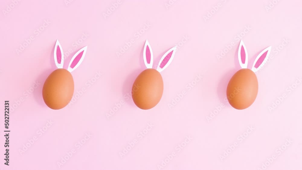 Easter eggs with rabbit ears appear on bright pink background and move. Easter concept. Stop motion flat lay Easter eggs with rabbit ears appear on bright pink background and move. Easter concept. Stop motion flat lay