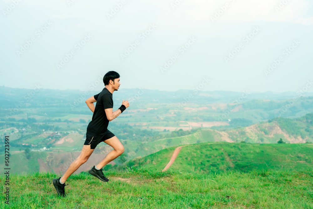 Young Asian runner, wearing black sportswear, running on a big mountain trail, cool morning, windmills, and sky in the background. Young Asian runner, wearing black sportswear, running on a big mountain trail, cool morning, windmills, and sky in the background.