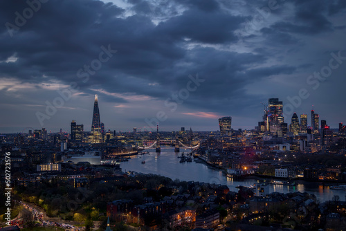 Panoramic view of the illuminated skyline of London with City, Tower Bridge and skyscrapers during a moody evening