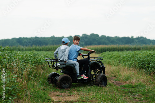 Two brothers driving four-wheller ATV quad bike. Happy children moments.