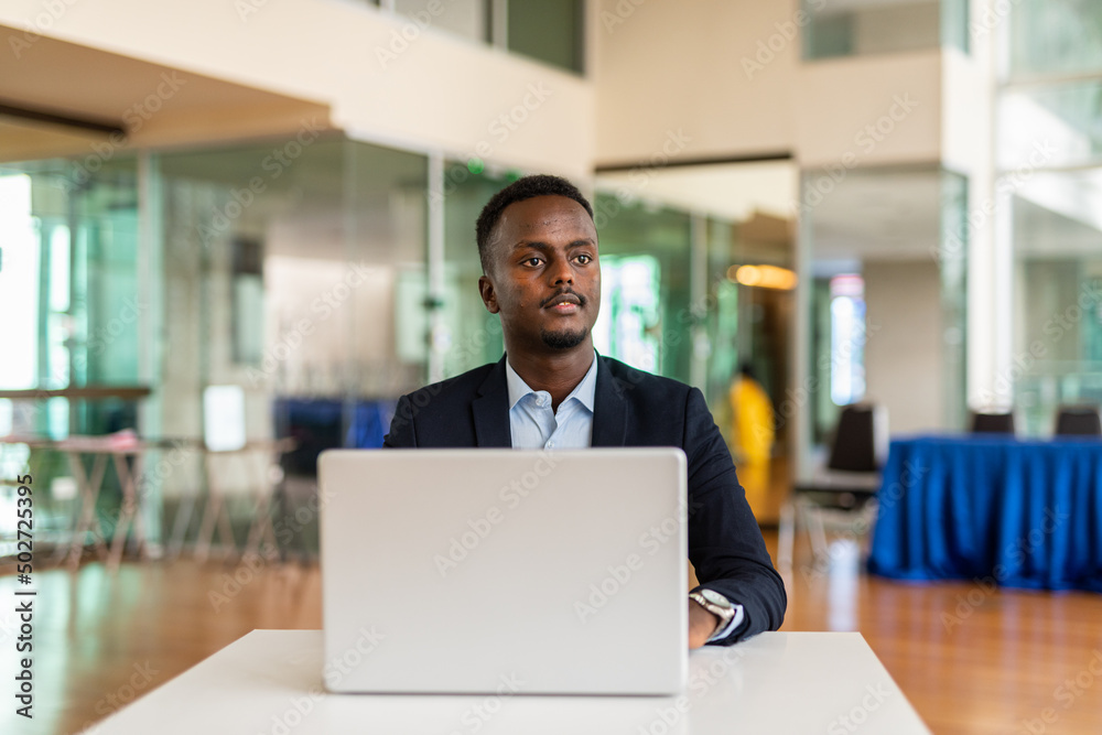 Portrait of young successful black businessman using laptop computer in office while thinking Portrait of young successful black businessman using laptop computer in office while thinking