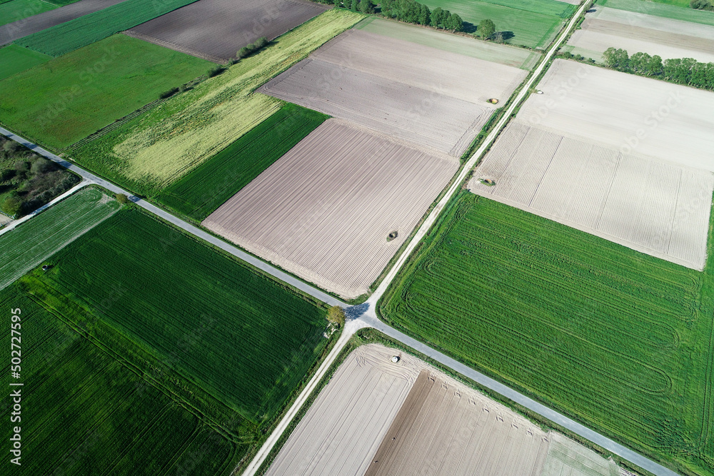 drone aerial view of some fields of rapeseed and cereal crops and two tractors plowing the soil.