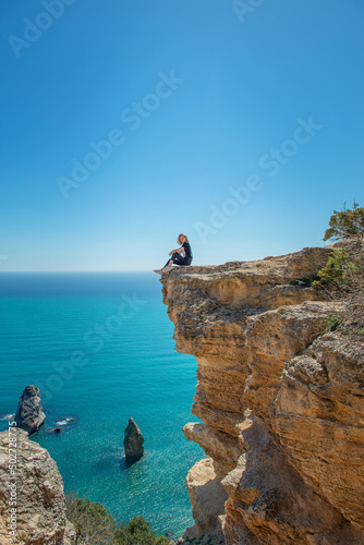 A girl is sitting on the edge of a cliff above a cliff near the Black Sea