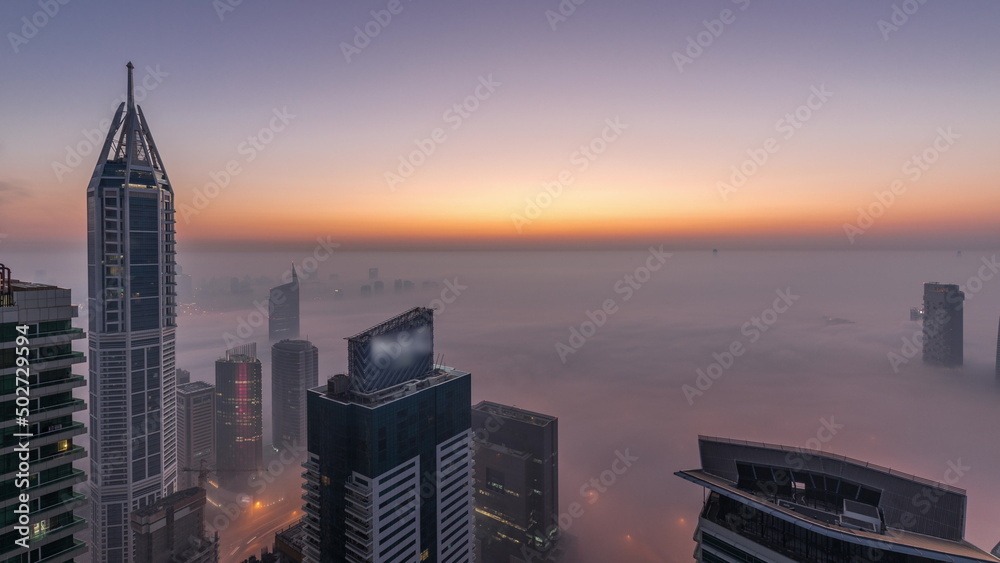 Rare early morning winter fog above the Dubai Marina skyline and skyscrapers lighted by street lights aerial night to day timelapse.