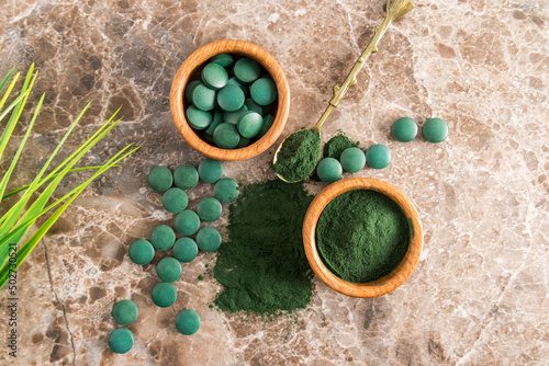 Green spirulina powder and tablets in wooden bowls on a brown marble background. a favorite superfood for vegetarians and athletes. top view.