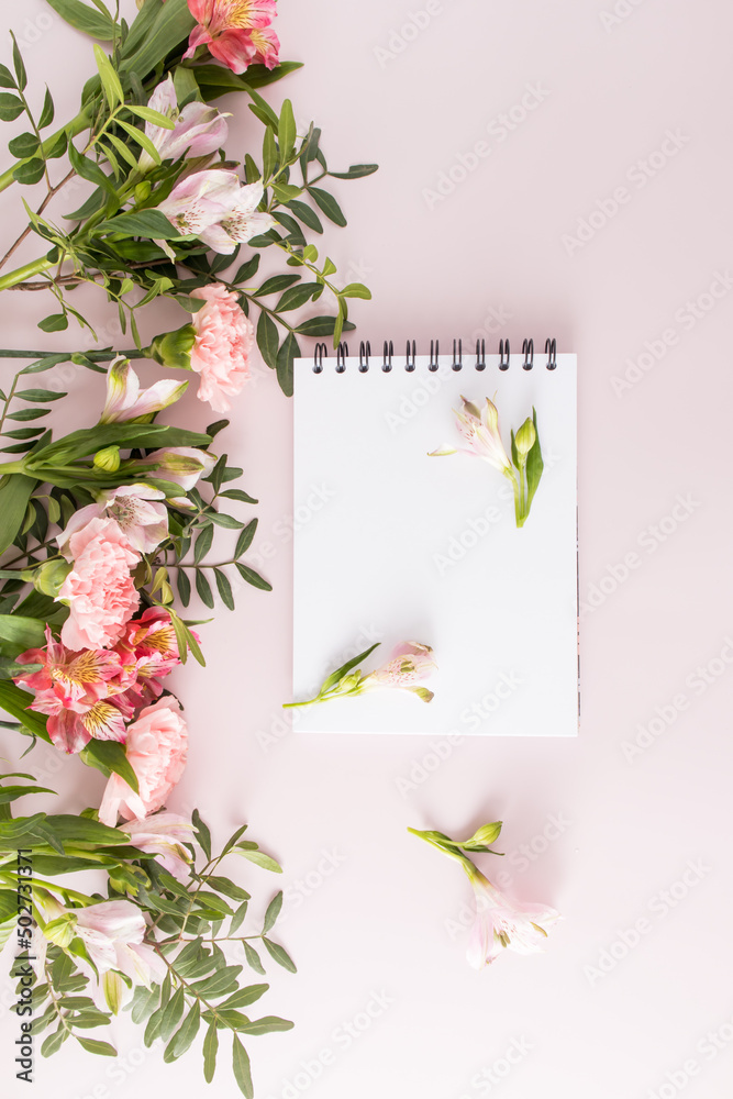 vertical top view of the blank white sheets of the notebook. pink pastel background with spring flowers. An empty layout for text.