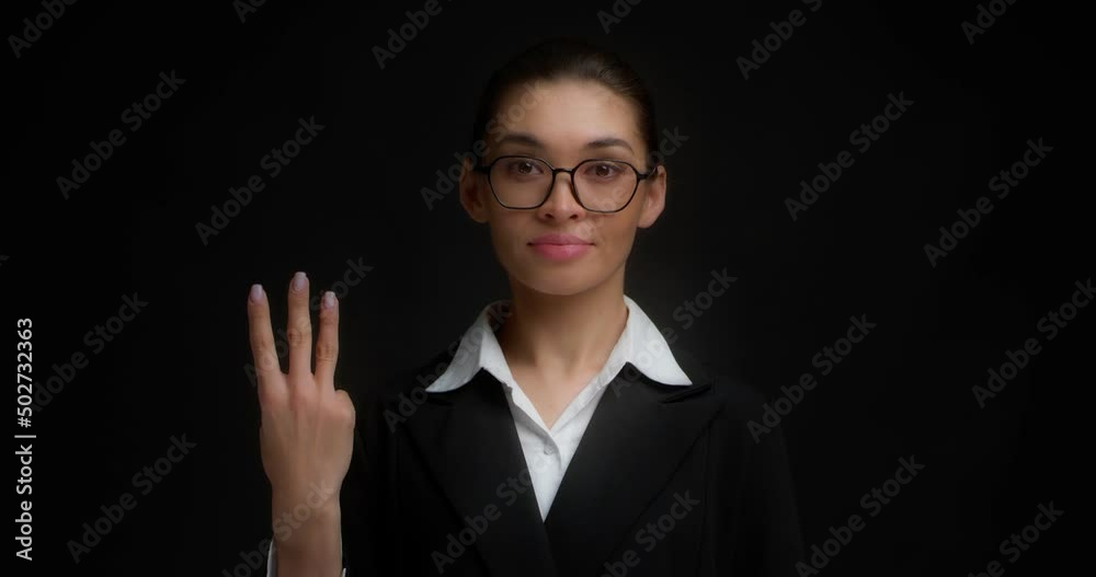 Business woman with glasses in business clothes with a serious face shows three finger with her right hand. Isolated on a black background. Business woman with glasses in business clothes with a serious face shows three finger with her right hand. Isolated on a black background.