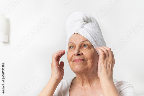 Caucasian senior woman with wrinkles with white towel takes care of her face