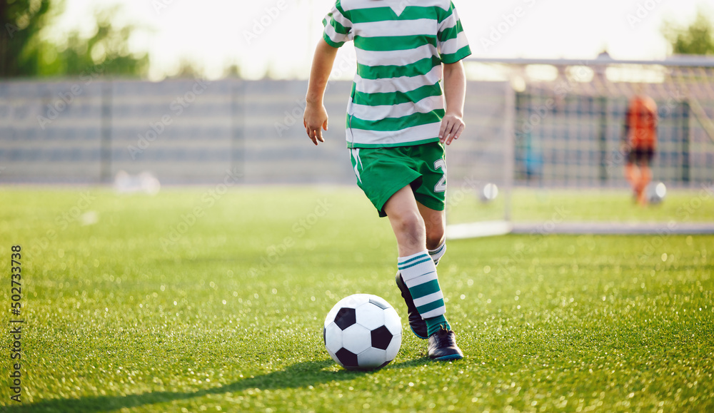 Obraz premium Football Player Running Ball Background. Low Angle Image of Soccer Boy Kicking Ball on Grass Training Field. School Boy in Striped Soccer Jersey Shirt