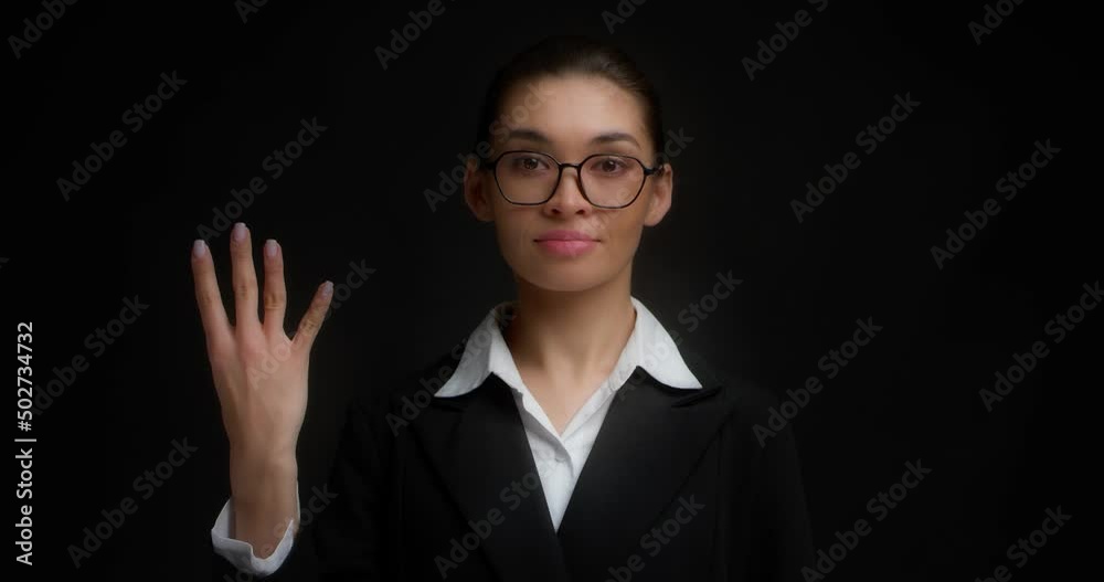 Business woman with glasses in business clothes with a serious face shows four finger with her right hand. Isolated on a black background.