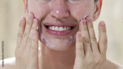 4k woman is applying day or night cream on face with fingers. young happy woman in mirror smiling with white natural teeth.excited pretty girl, rosaceae, brown spots on face. no eyes, unrecognisable 