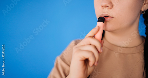 A random pretty woman standing and about to hover on a blue background in the studio. the concept of vaping and modern smoking