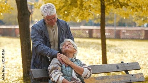 Elderly caucasian heterosexual couple at their favourite park. Amazing affection between two senior retired people. Protective husband touches his beloved wife's arm. High quality photo