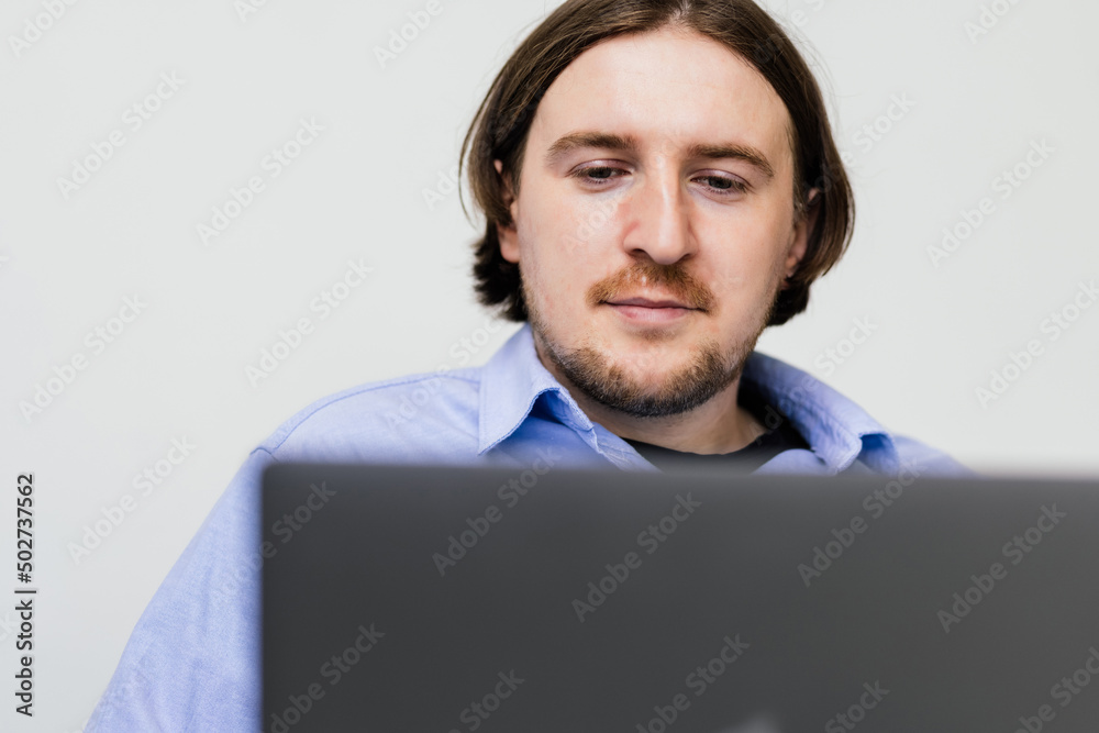 Portrait of young bearded man smiling and using laptop while sitting on sofa at home Portrait of young bearded man smiling and using laptop while sitting on sofa at home