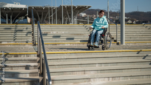 A caucasian woman in a wheelchair cannot go down stairs without a ramp. Hard to access environment. 
