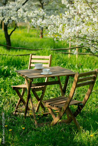 Cup of coffee or tea on wooden table next to blooming tree in a garden
