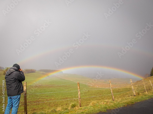 man taking photos of a double rainbow on the aubrac plateau lozere France in the rain . photo