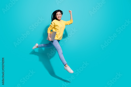 Full length photo of funny lucky lady dressed yellow sweater jumping runnig gadget empty space isolated turquoise color background photo