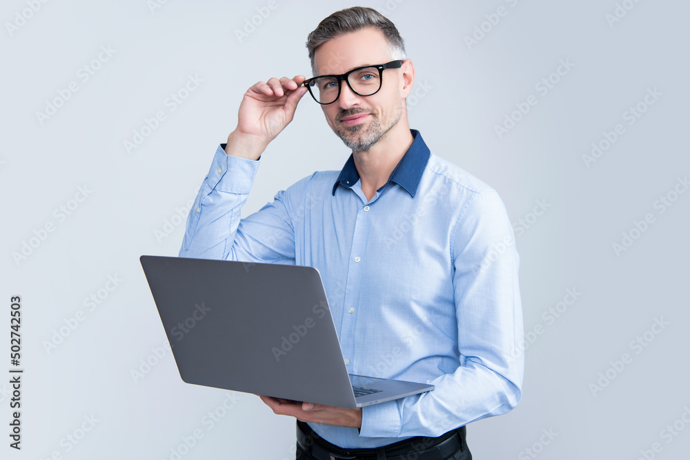 mature entrepreneur in eyeglasses working on computer on grey background