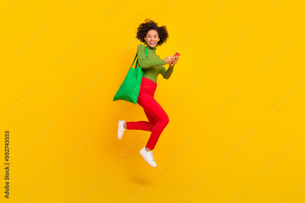Full body profile side photo of young cheerful girl jump active use mobile order purchase store isolated over yellow color background