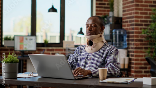 Fotografia Financial analyst with physical injury wearing medical neck collar at office job, using cervical foam to treat vertebrae accident