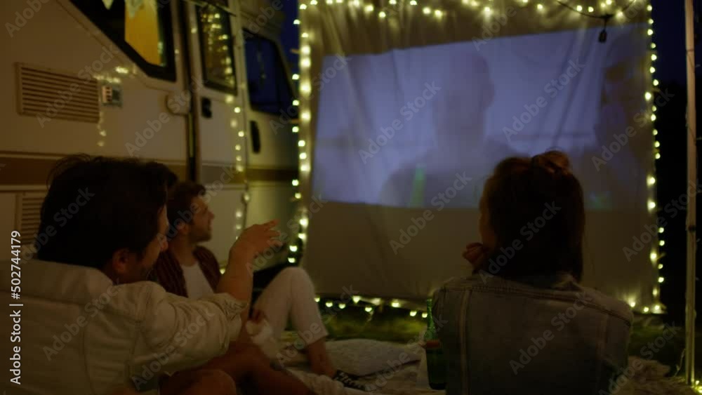Group of young cheerful people watching a movie on camping site on projection screen. Shot with RED helium camera in 8K  