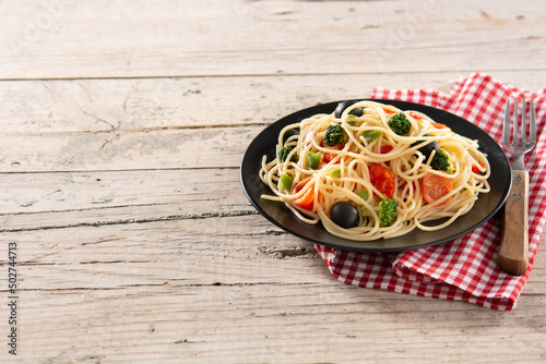 Spaghetti with vegetables(broccoli,tomatoes,peppers) on wooden table. Copy space