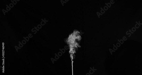 Slow motion single stream of smoke erupting from the bottom middle of frame that slowly drifts rightwards. Shot on black for easy composting.