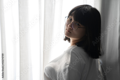 Free Download Asian Thai Chinese Woman with her black glasses stands in front of white curtain with the light from outside. It's a cute sexy shot image. - GFXLoad