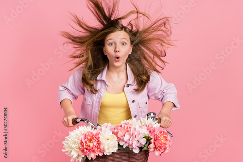 Photo of shocked amazed lady ride bicycle wind blow hair open mouth wear jacket isolated pink color background
