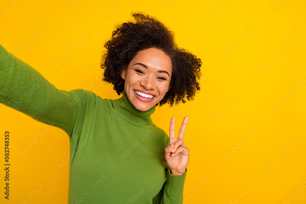 Photo of young lovely lady show fingers peace hello v-symbol make selfie isolated over yellow color background