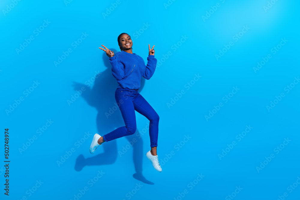 Photo of excited shiny woman wear sweatshirt jumping showing v-sign empty space isolated blue color background
