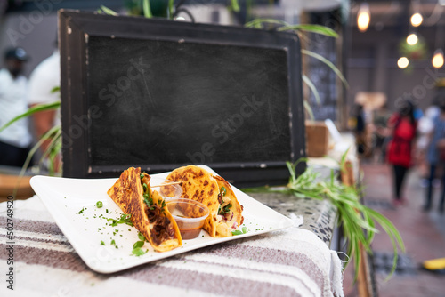 An empty chalkboard at a market with soft shell tacos in foreground - copy space photo
