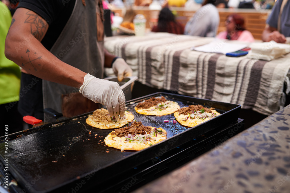 Close up of chef hands sprinkling onions onto tacos on a grill