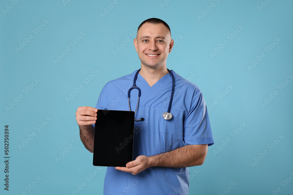 Doctor with stethoscope holding blank tablet on light blue background, space for design. Cardiology concept