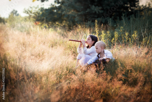 Dzieci grają na instrumentach siedząc na łące w wysokiej trawie, dziewczynka gra na flecie photo