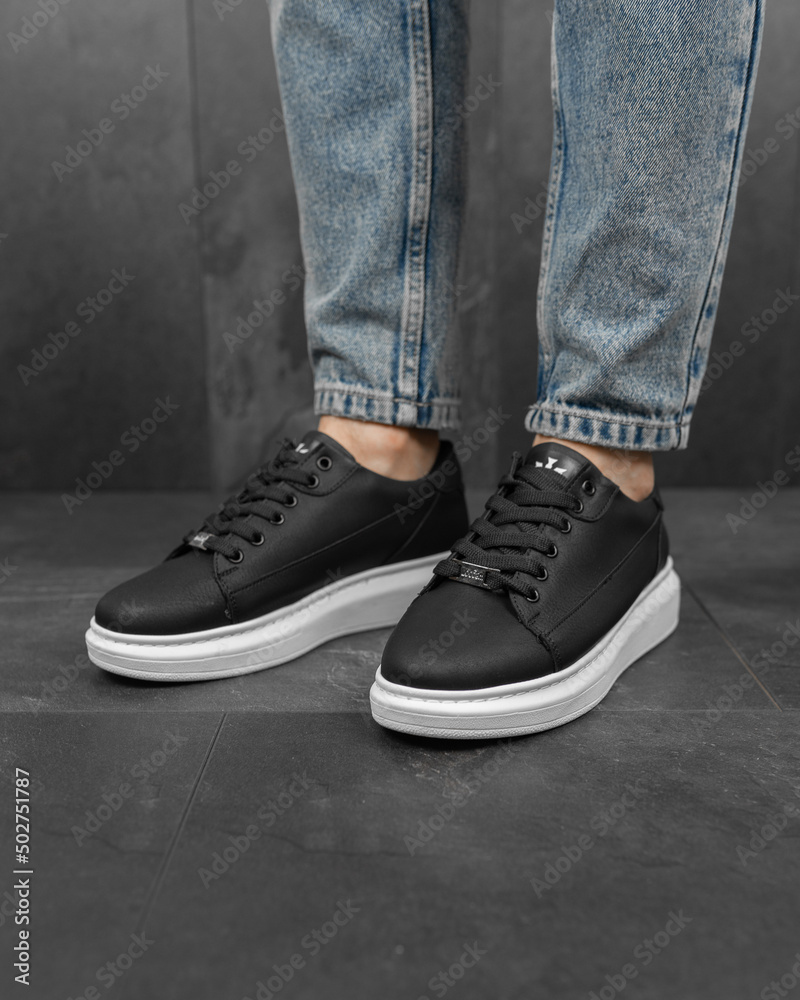 Close-up photo of men's black sneakers with jeans. White sneakers on his feet Close-up photo of men's black sneakers with jeans. White sneakers on his feet