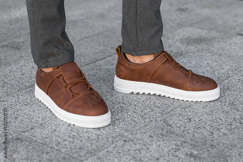 Close-up photo of men s legs with leather brown sneakers. Genuine leather shoes with white soles. Sneakers for businessmen.