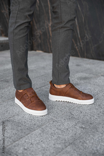 Close-up photo of men's legs with leather brown sneakers. Genuine leather shoes with white soles. Sneakers for businessmen.